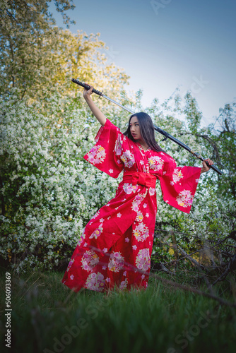 Girl in the red kimono with the katana sword in the apple garden concept.