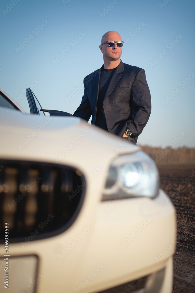 Fototapeta premium Driver in the suit stands in the field on the empty country side road.