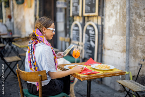 Woman eating italian pasta and drinking wine at restaurant on the street in Rome. Concept of Italian gastronomy and travel. Stylish woman with sunglasses and colorful hair shawl