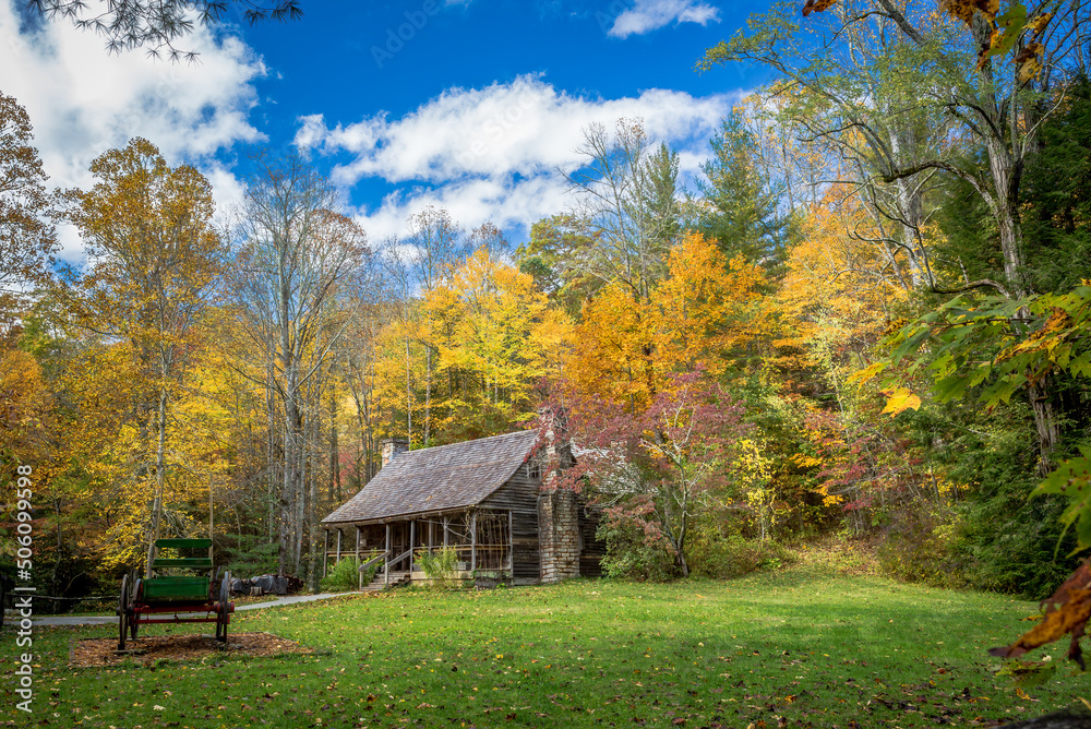 Colorful fall autumn leaves of yellow and orange surround a small cabin in the woods.