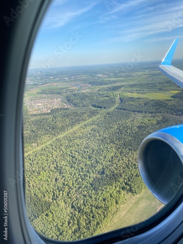 Panorama from the airplane window: green forests and fields on a sunny day.