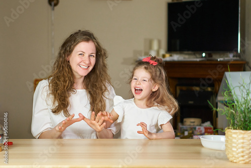 Have fun together. Smile and laugh at home. Happy family at table. Motherhood is joy. Children laughter. Kid play. woman babysitter is good for sister. White dresses on caucasian women. tickles girl