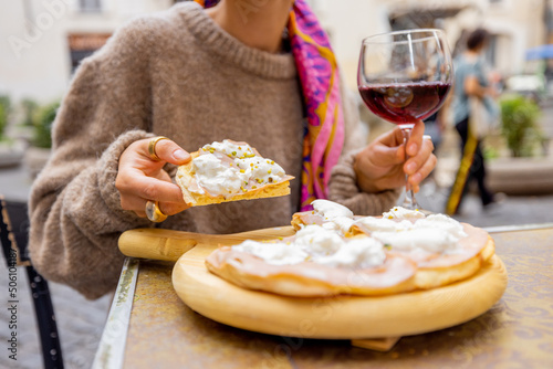 Woman holding pizza and a glass of wine at outdoor restaurant. Concept of Italian gastronomy and travel. Close-up