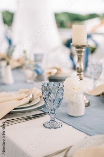 Long dinner tables covered with white cloth, served with porcelain and blue glasses and rich decorated with flowers 