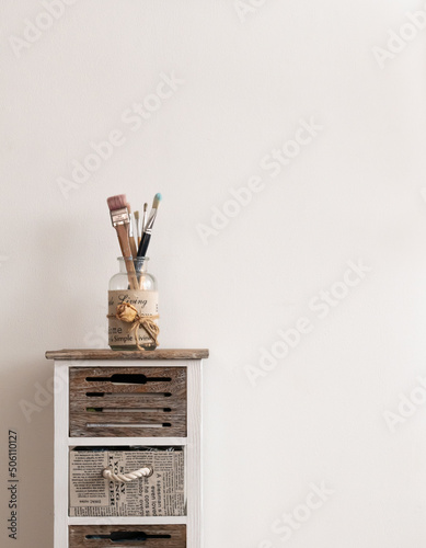 Glass jar with wooden paintbrushes on beautiful vintage table against warm white wall