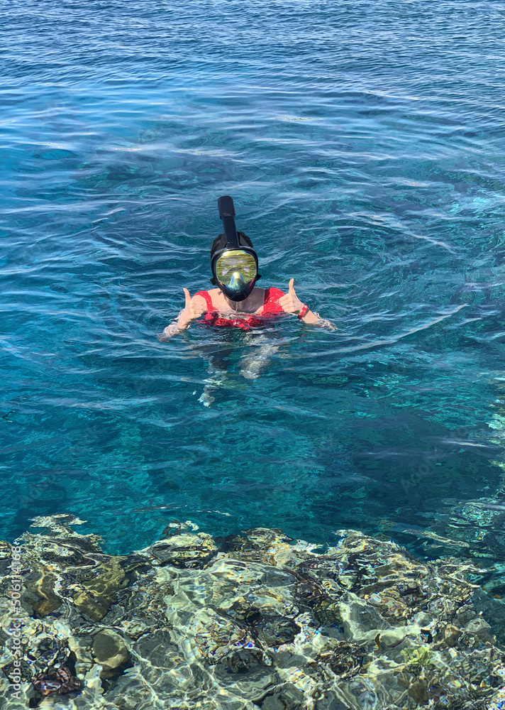Happy young woman swims in a mask. Snorkeling, fish watching.