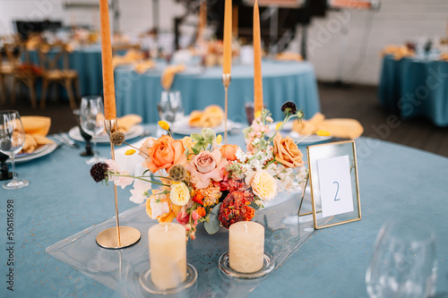 Cozy outdoor Wedding. Banquet. Chairs and honeymooners table decorated with candles, served with cutlery and crockery and covered with a blue tablecloth.  photo