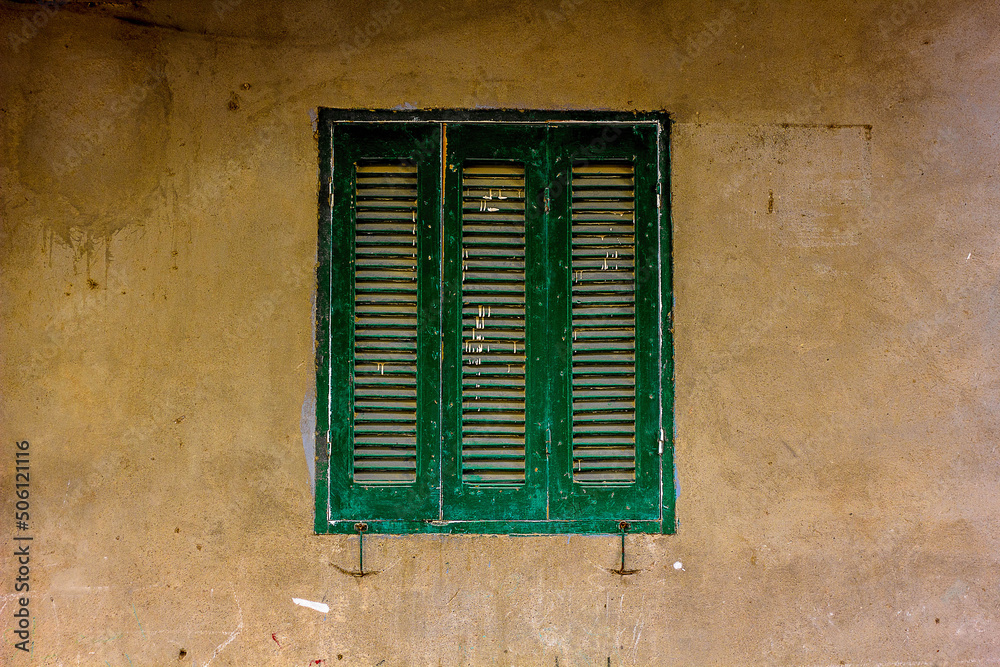Old wall with dirty plaster. Old window with shutters.