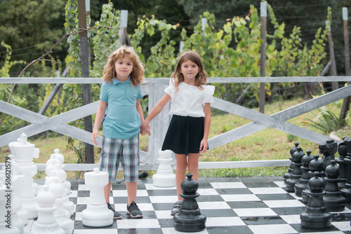 Brother and sister playing on big chess board. Little boy and girl kids enjoying spring. Kids walking at backyard. Best friends two children play chess.