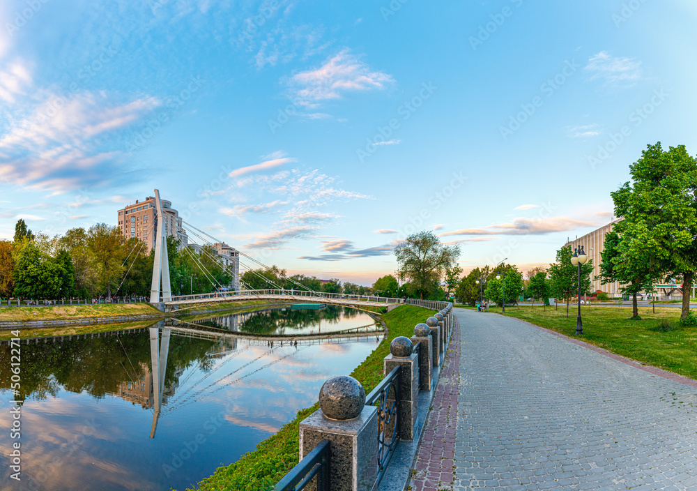 Fototapeta premium Bridge of Lovers across the Lopan River. Square Strelka. Evening lighting. City landmark and promenade area. Kharkiv city, Ukraine