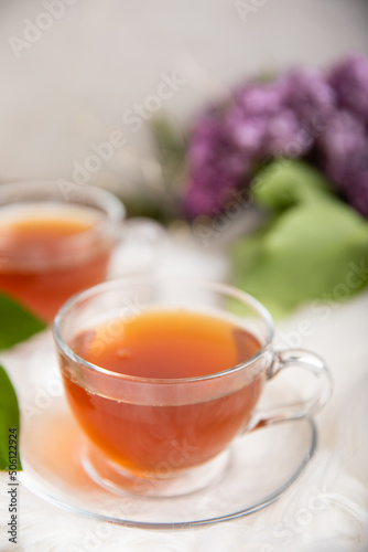 A cup of green tea against the background of a spring bouquet of lilacs on a white texture wood. Romantic composition with books and candles. spring tea drink. Place to copy. Romantic concept.