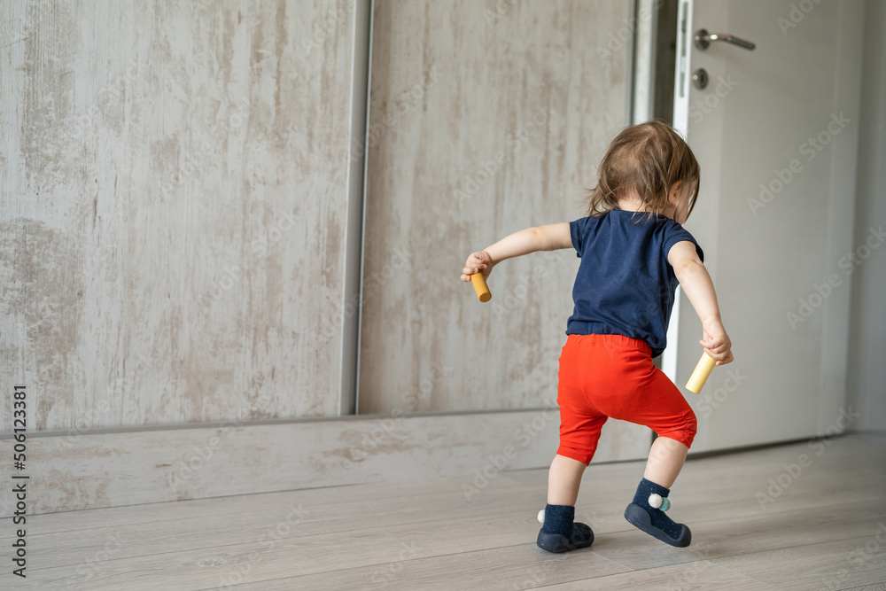 Back view full length of one small toddler caucasian boy or girl waking going out while holding toys in hands copy space childhood development and growing up concept