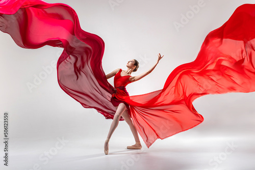 Ballerina in red leotard dancing in white studio room with red clothes waving around