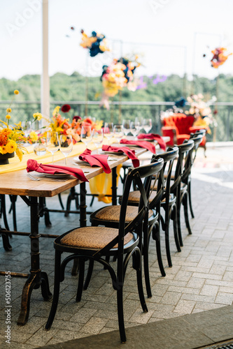festive tables and chairs, tables decorated with compositions of flowers and candles. Yellow tablecloth. Pink napkin On the tables are glasses, plates and cutlery