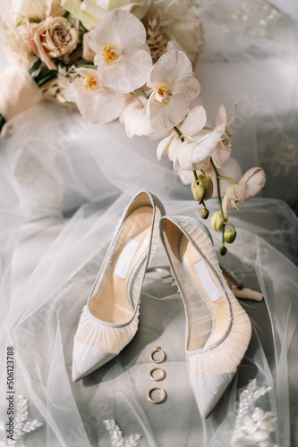 Stylish luxury shoes with lace floral pattern . Modern wedding shoes on tulle in soft morning light. Bridal morning preparations and boudoir. Flat lay