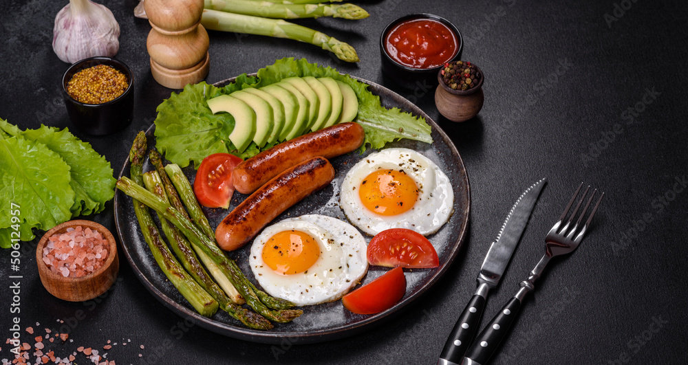 A delicious nourishing breakfast with fried eggs, sausages, asparagus, tomatoes, avocado, spices and herbs