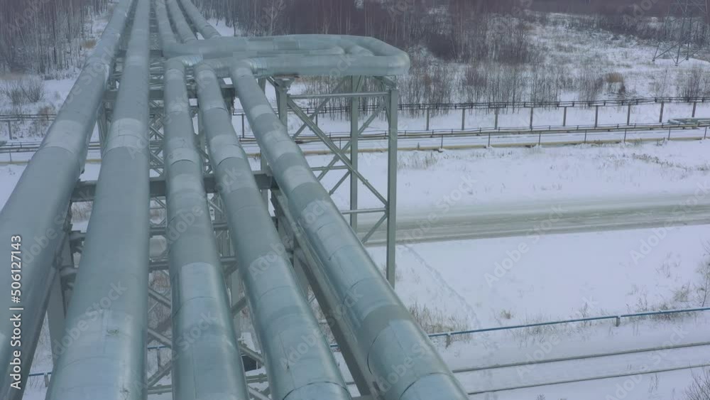 Shiny metal pipelines over empty road at gas and oil refinery plant during snowstorm on winter day close aerial view