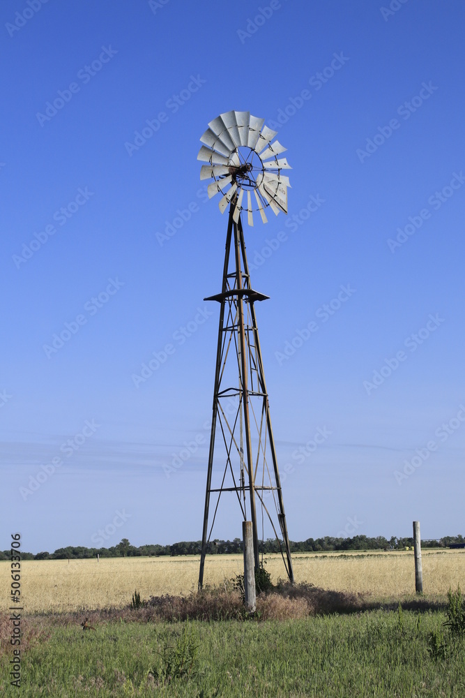 Kansas Country Windmill in a farm field with green grass and blue sky out in the country west of Nickerson Kansas USA.