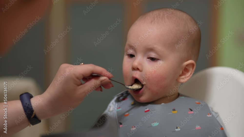 Mother feeding baby boy in high chair. Mother feeds her little son from a spoon. Mother feeding baby boy in high chair. Mother feeds her little son from a spoon.