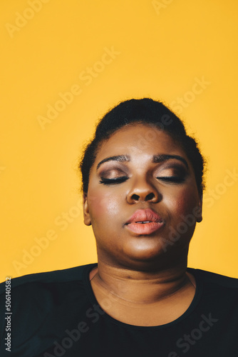 closeup portrait of a thoughtful beautiful young adult african american woman with eyes closed afro hairstyle on yellow background studio © Carlos David