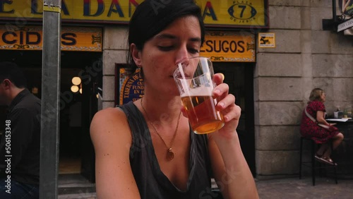 Beautiful Caucasian woman drinks beer in a bar in Madrid (Spain). Spanish girl sitting on a terrace enjoying a beer. 4K summer. Woman enjoying a beer in Spain. photo