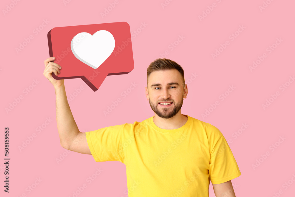 Handsome young man holding speech bubble with heart on pink background. Concept of LIKE Handsome young man holding speech bubble with heart on pink background. Concept of LIKE