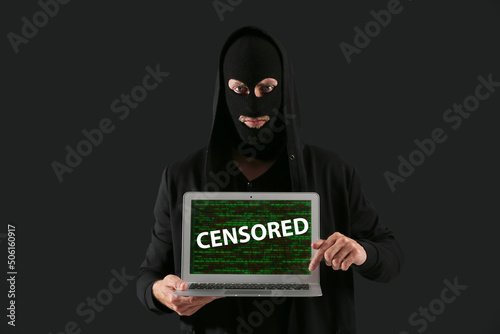 Male hacker holding laptop with word CENSORED on screen against dark background