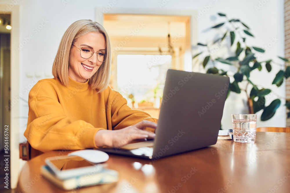 Cheerful mature woman working sitting at dinning table working from home office Cheerful mature woman working sitting at dinning table working from home office