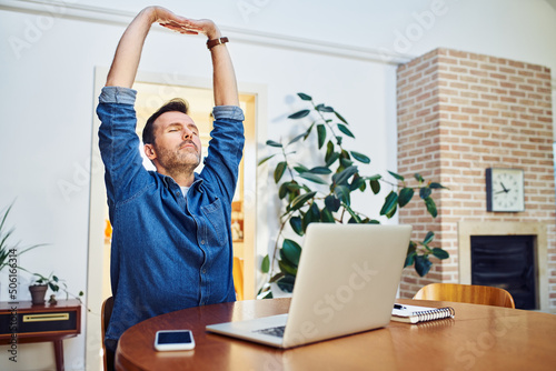 Man stretching his arms while working on laptop at home