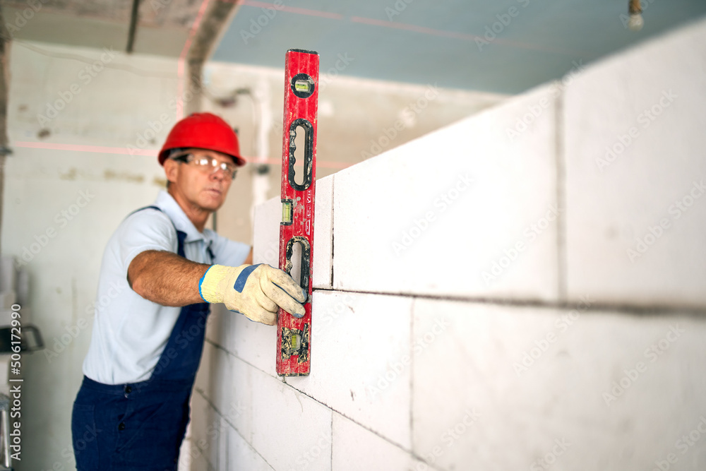 Bricklayer using spirit bubble and laser level to precise check concrete blocks on wall. Contractor uses tools for brickwork. Worker constructs a wall in new apartment real estate. Bricklayer using spirit bubble and laser level to precise check concrete blocks on wall. Contractor uses tools for brickwork. Worker constructs a wall in new apartment real estate.