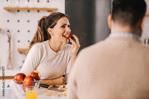 Obraz na plátně A woman eating apple in kitchen at home and smiling at boyfriend.