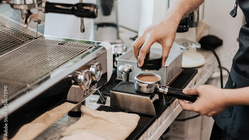 Barista using a tamper to press ground coffee into a portafilter. Close-up view on barista hands to making coffee with coffee machine. Coffee owner concept.