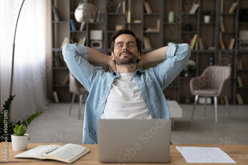 Meeting friday. Happy young guy freelancer enjoy calm moment when task is done relax rest stretch back hold hands over head. Serene millennial man recline on chair with closed eyes take break in work