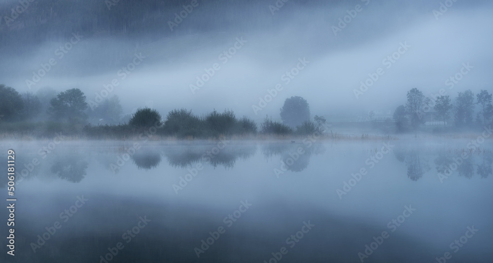 Autumn mist by the lake with beautiful calm reflections.