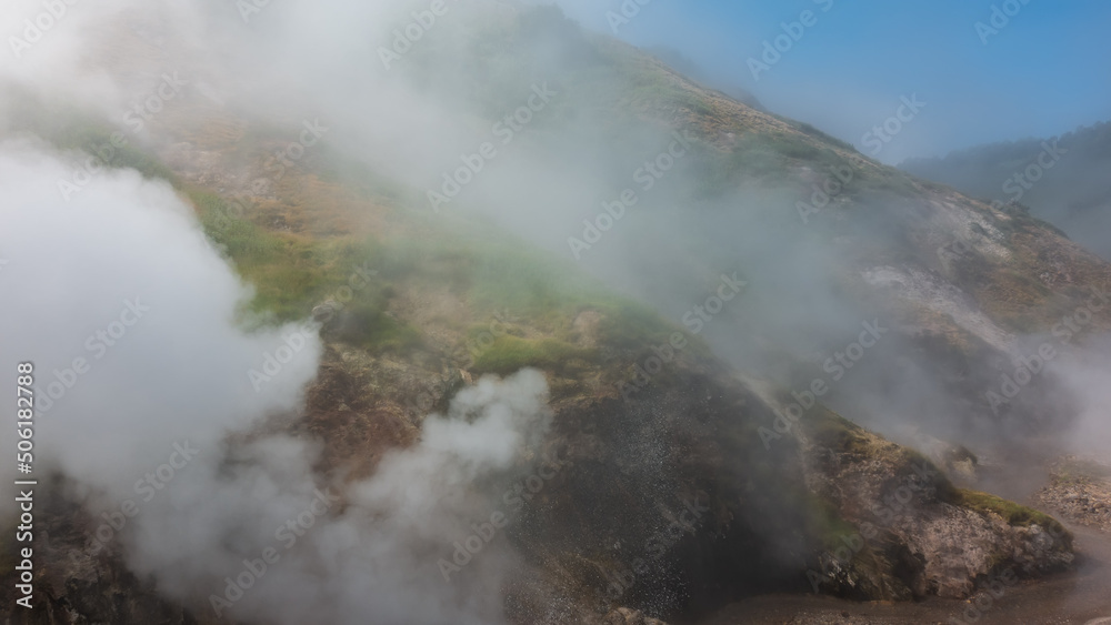 Fototapeta premium The hillside is shrouded in thick steam from an erupting geyser. Poor visibility due to haze. Kamchatka. Valley of Geysers
