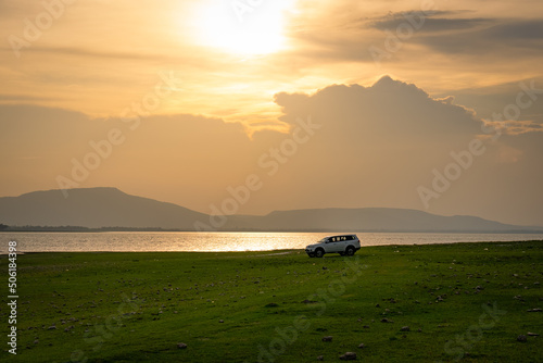 Car was Drived on Green Meadow Near Lake at Sunset During Summer Vacation photo