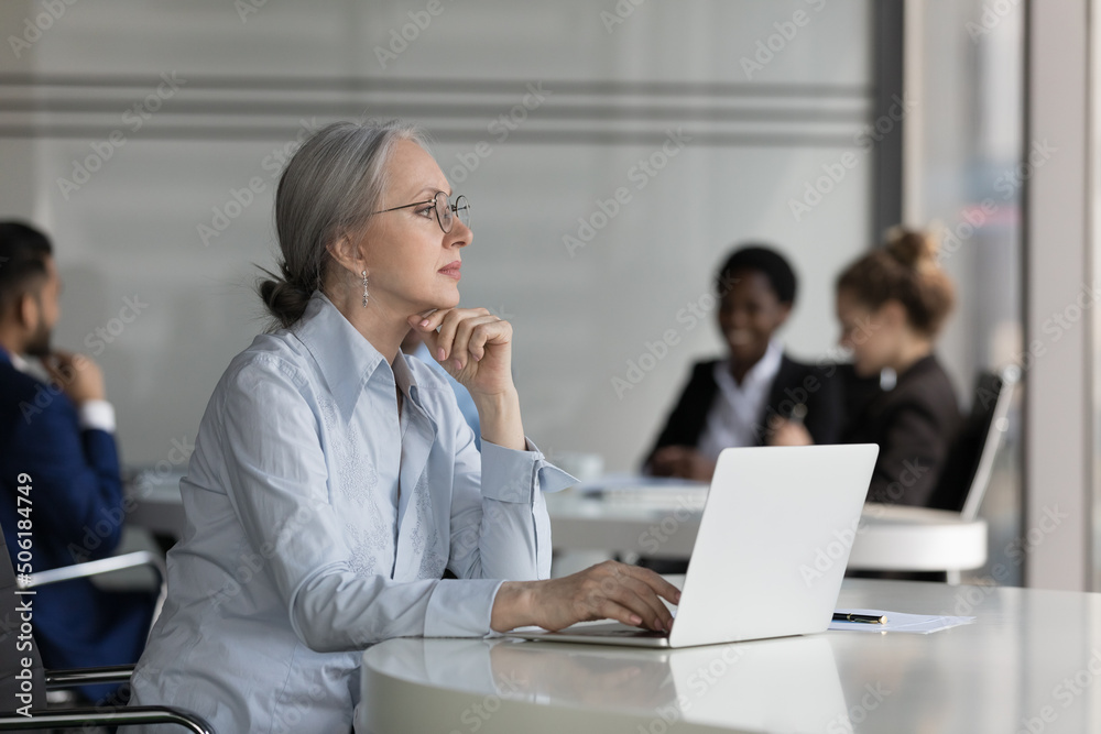 Thoughtful middle-aged businesswoman sit at desk with laptop looks into distance, search business solution, faced up with challenge, thinks working over on-line task, corporate office workflow concept Thoughtful middle-aged businesswoman sit at desk with laptop looks into distance, search business solution, faced up with challenge, thinks working over on-line task, corporate office workflow concept