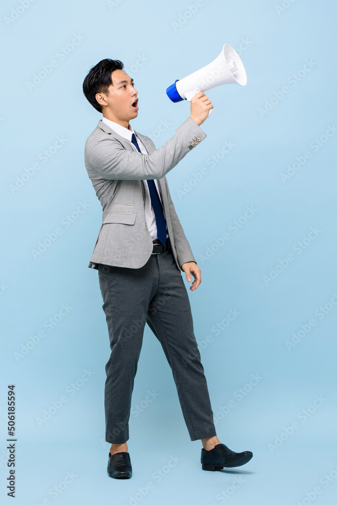 Young handsome Asian man in formal business suit holding megaphone in isolated light blue color studio background Young handsome Asian man in formal business suit holding megaphone in isolated light blue color studio background