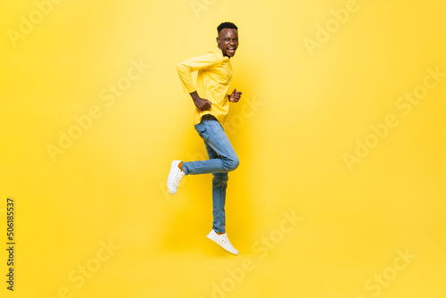 Full length portrait of excited African man jumping in isolated yellow color studio background