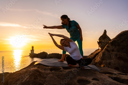 A yoga instructor working with the student in nature by the sea at sunset, healthy and naturist life, outdoor pilates