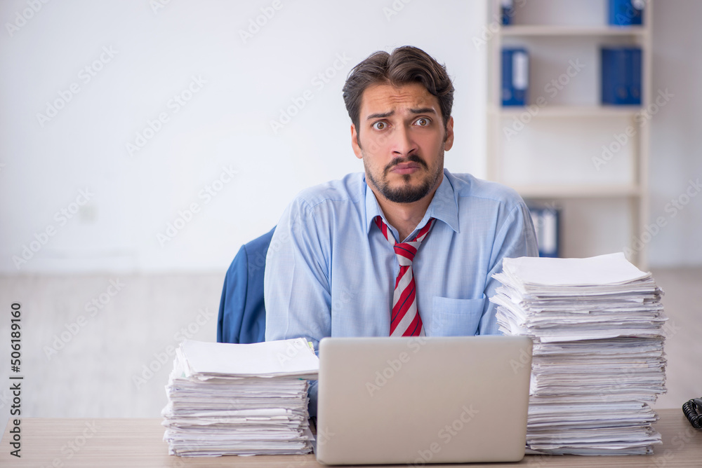Young male employee and too much work in the office Young male employee and too much work in the office