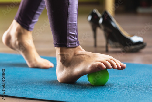 A woman performs relaxing exercises of the muscles of the foot with a massage ball, for the prevention of leg fatigue after wearing high-heeled shoes