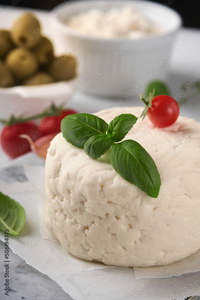 Ricotta cheese. Homemade Ricotta cheese with basil, garlic, tomatoes and green olives on parchment paperback and stand. Italian food. Selective focus. Ricotta cheese. Homemade Ricotta cheese with basil, garlic, tomatoes and green olives on parchment paperback and stand. Italian food. Selective focus.