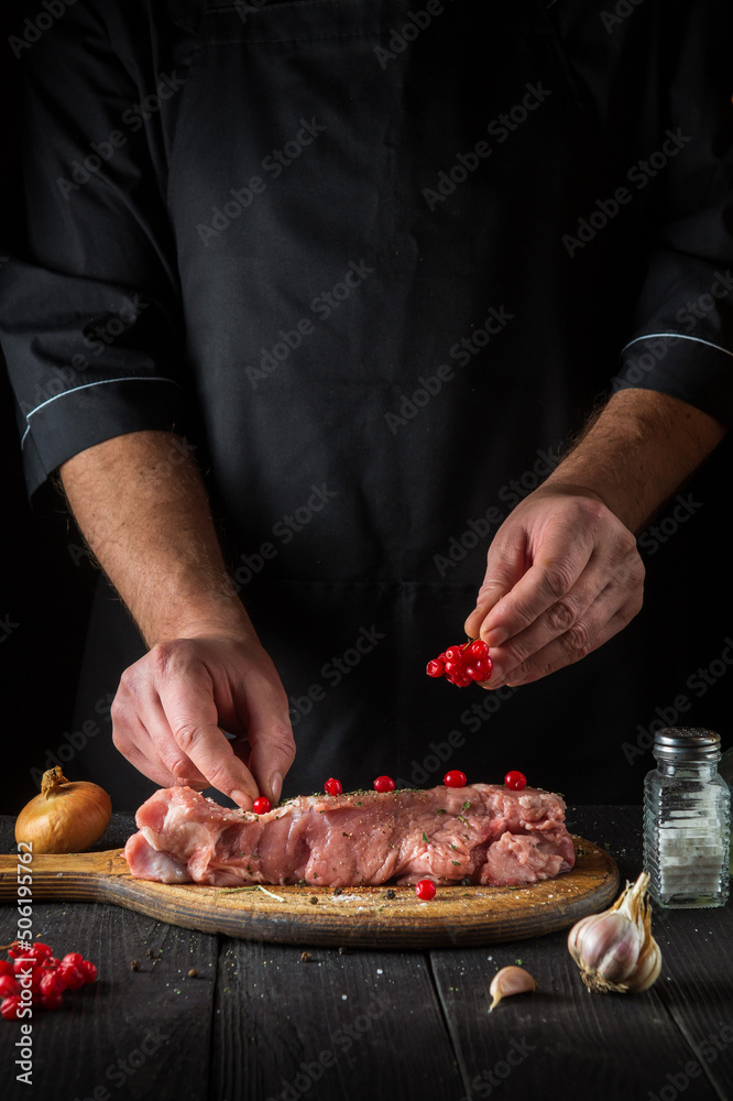 In the restaurant kitchen chef prepares raw calf meat. Before baking, the cook puts the viburnum on the beef. National dish