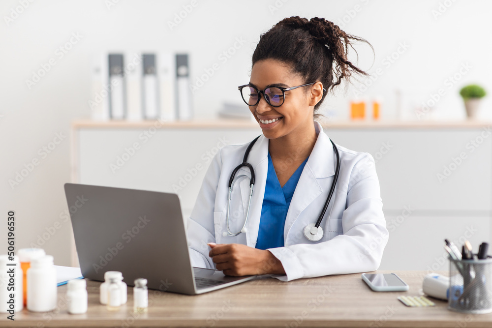 Portrait of smiling doctor looking at screen sitting at desk Portrait of smiling doctor looking at screen sitting at desk