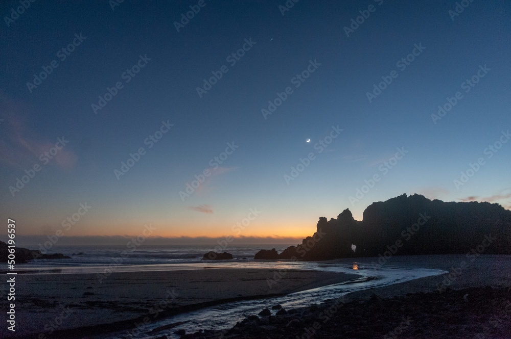 A cresent moon accentuates the beach during the golden hour after sunset.