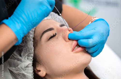 Cosmetic procedure for non-surgical rhinoplasty. The beautician inserts cosmetic threads into the nose with a needle to reshape the nose, close-up. Plastic surgery, cosmetology