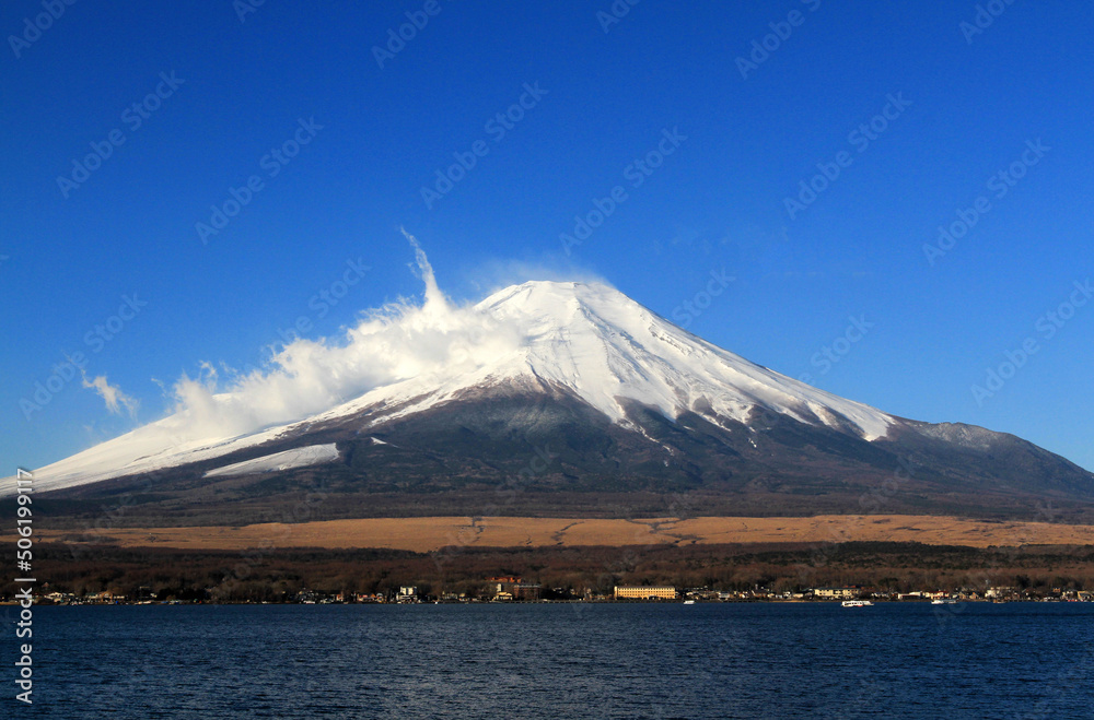 Fuji mountain with snow and fog covered top, lake or sea and clear blue sky background with copy space. This place famous in Japan and Asia for people travel to visit and take picture.