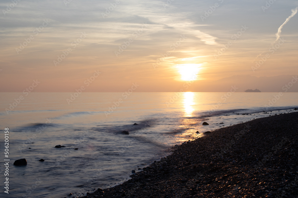 sunrise or sunset of a beach with stones in the water and on the shore long exposure photo with the reflection of the sun on the stones on the shore and small silky waves