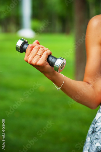 Sports girl holding a dumbbell in her hand at a workout in the park